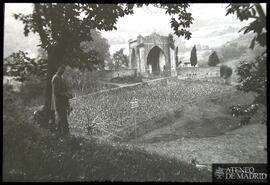 Vista de campo con hombre en primer plano y cementerio al fondo